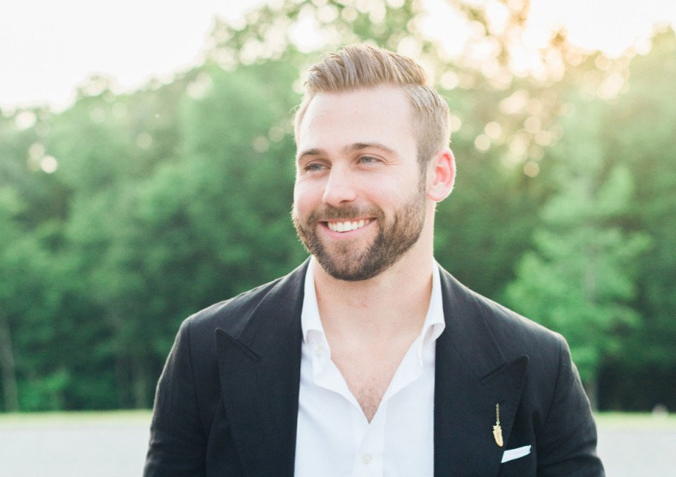 een man met een baard en een wit shirt en zwarte jas