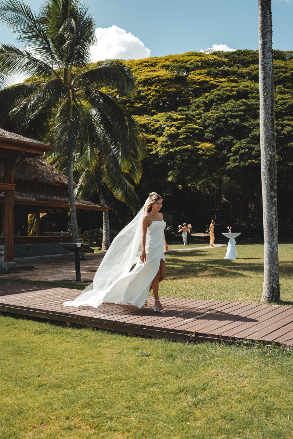 een bruid die op een houten loopbrug loopt voor palmbomen