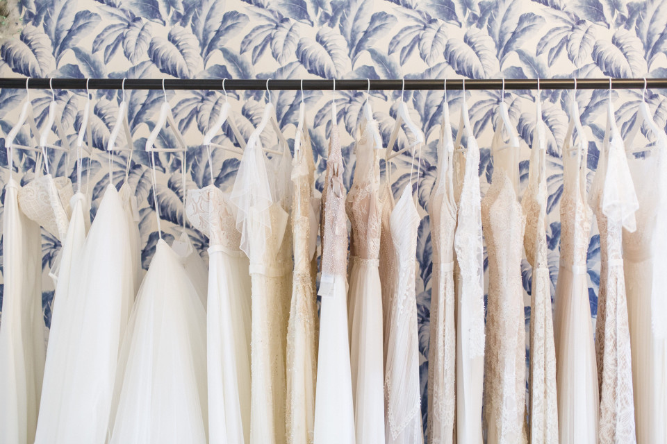 een trouwjurk hangend aan een rek voor een blauw en wit bloemenbehang
