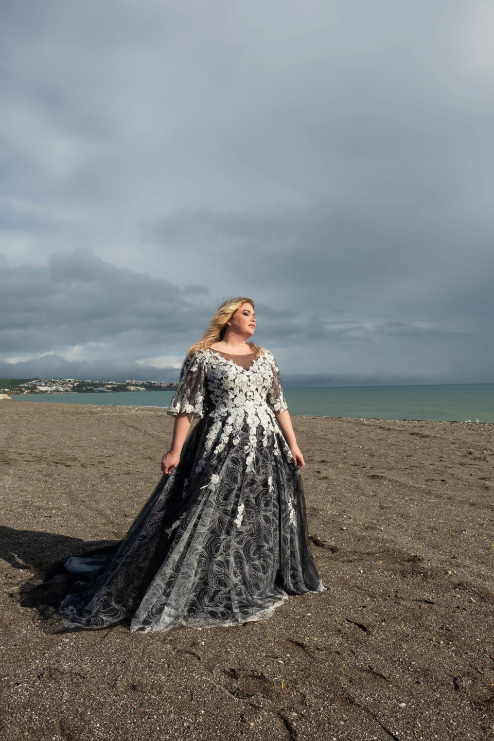 een vrouw in een zwart-witte jurk die op het strand staat