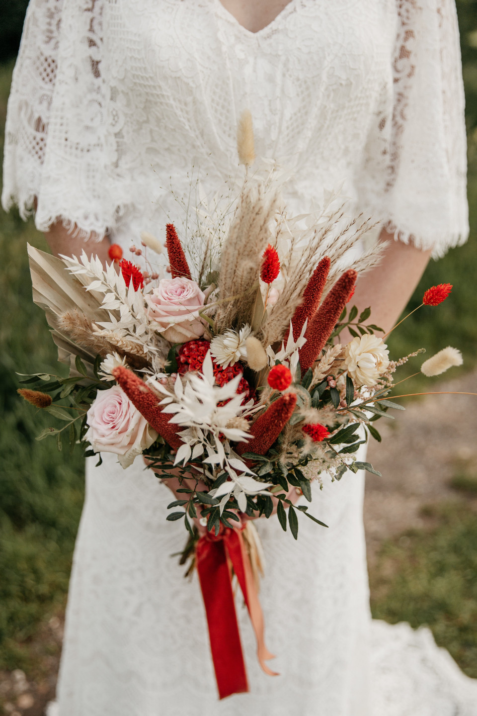een bruid die een boeket gedroogde bloemen en een rode strik vasthoudt