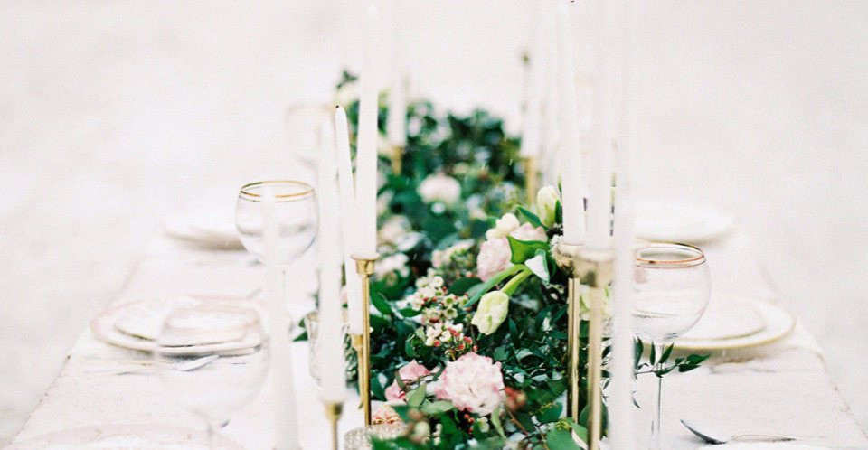 een lange tafel met witte en gouden kaarsen en bloemen
