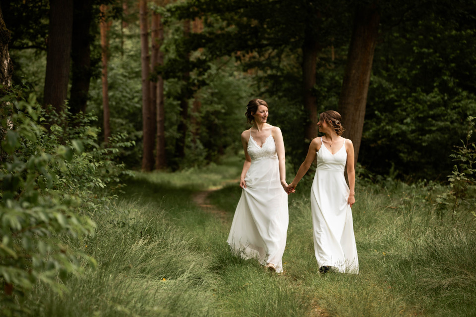 twee bruiden die hand in hand door het bos lopen