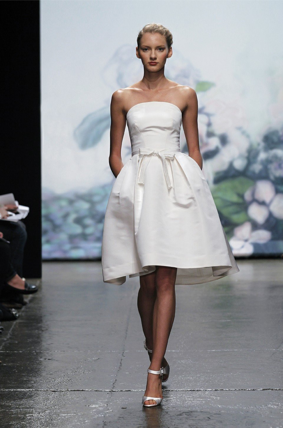 een model loopt op de catwalk in een witte jurk
