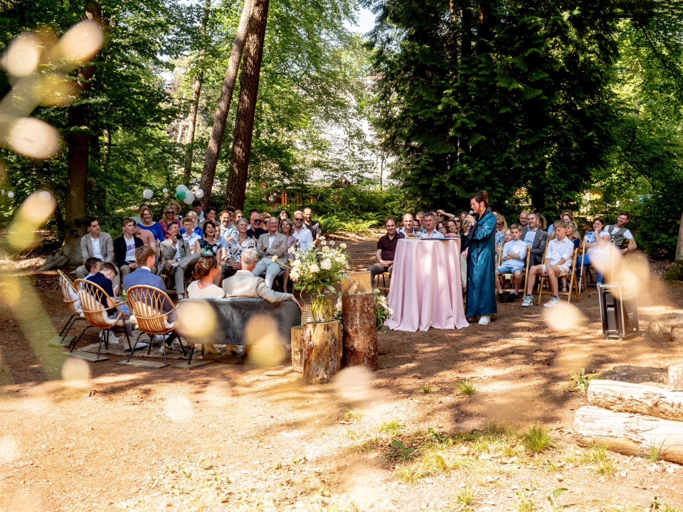een bruiloftsceremonie in het bos met mensen die aan tafels zitten