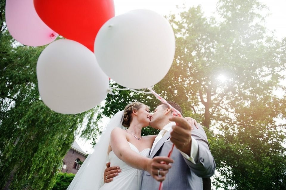 een bruid en bruidegom kussen terwijl ze rode en witte ballonnen vasthouden
