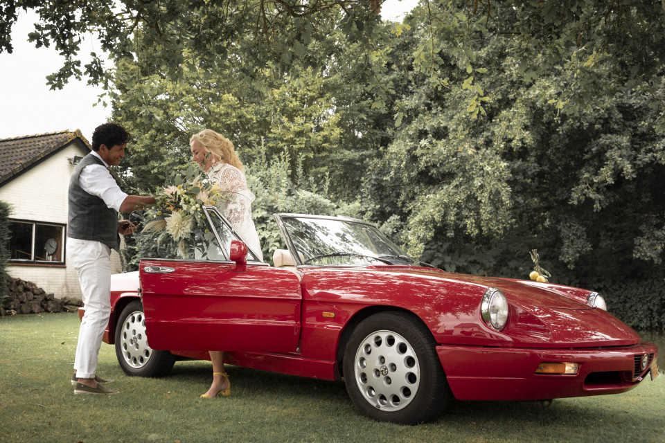 een man en vrouw die naast een rode cabriolet staan