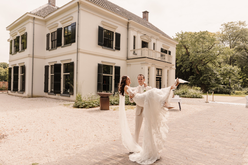 een bruid en bruidegom die voor een groot wit huis staan