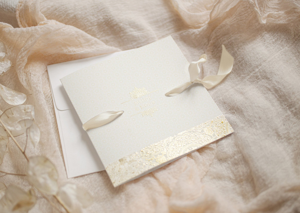 een trouwkaart met gouden lint en een witte envelop