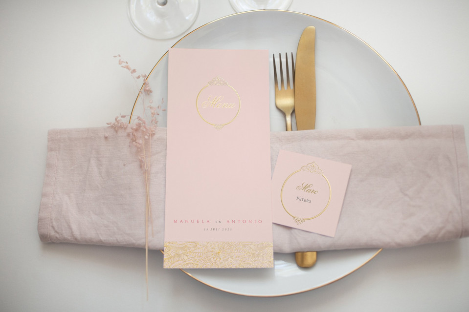 een roze tafelsetting met gouden servetten en een plaatskaart