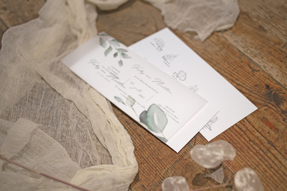 een trouwuitnodiging met een witte envelop en een groen blad