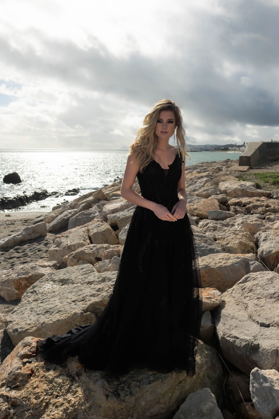 een vrouw in een zwarte jurk die op rotsen bij de oceaan staat