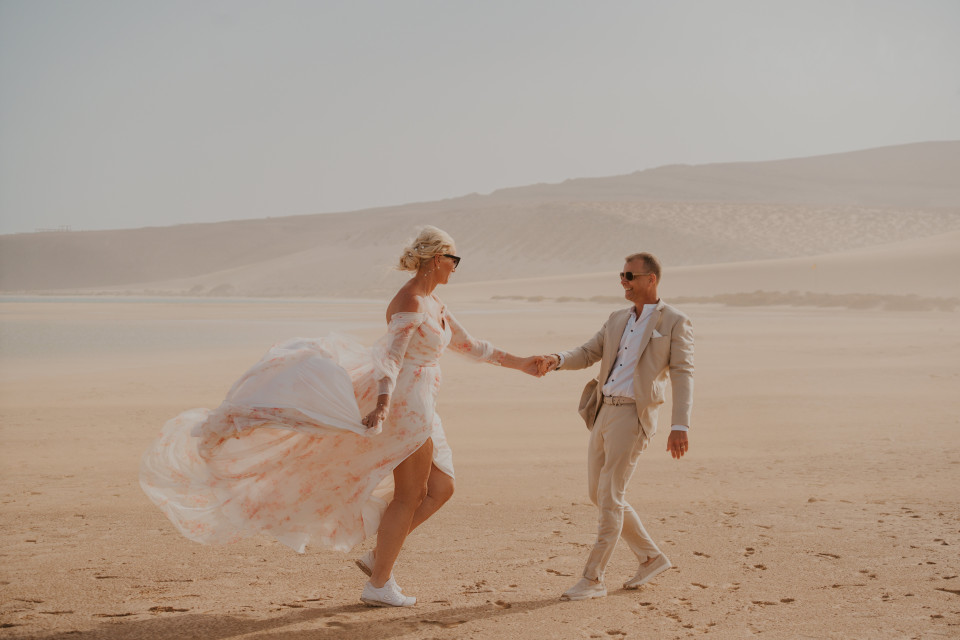 een man en een vrouw die hand in hand op het strand lopen