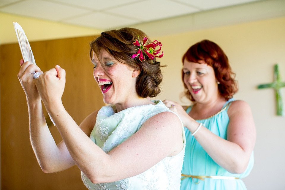 twee vrouwen lachen terwijl een van hen een trouwjurk vasthoudt