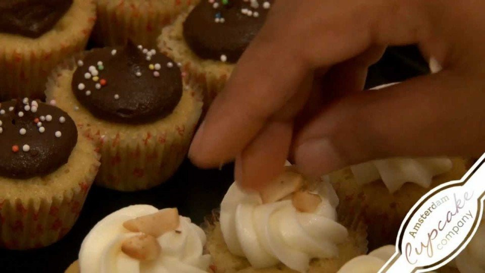 een persoon plaatst een stuk chocolade glazuur op een cupcake