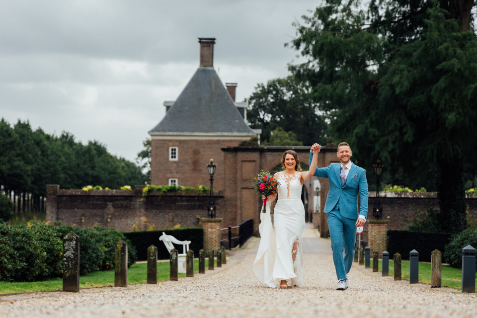 een bruid en bruidegom die over een pad voor een kasteel lopen