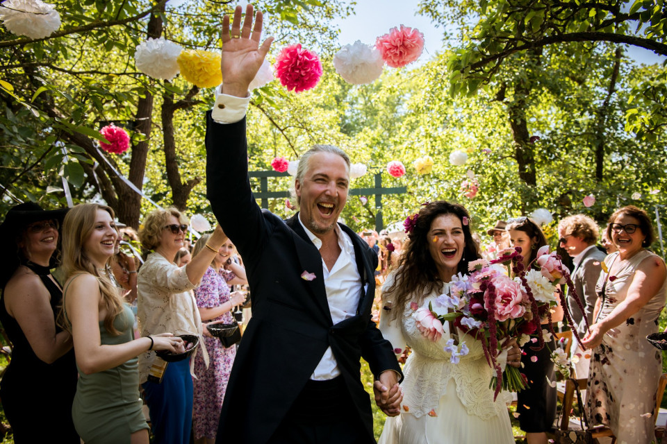 een bruid en bruidegom lopen door het bos met papieren pom poms