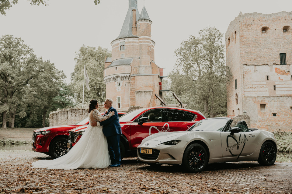 een bruid en bruidegom poseren met hun sportauto's voor een kasteel