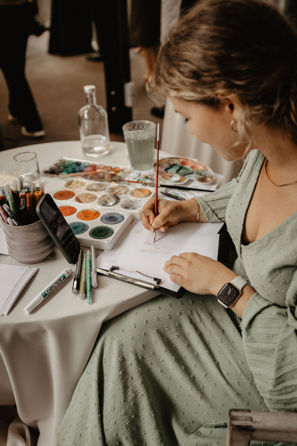 een vrouw die aan een tafel zit met aquarellen erop