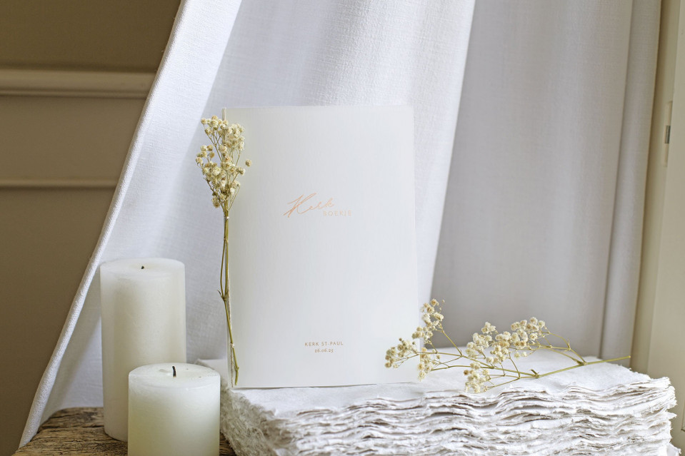 een witte kaars, een boek en een wit servet