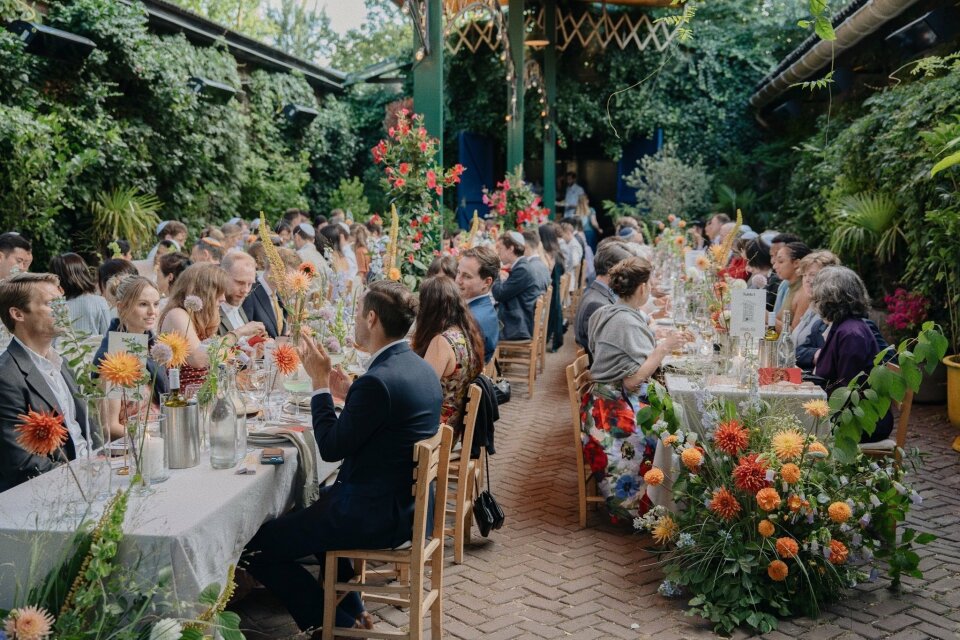 een grote groep mensen die aan tafels in een tuin zit