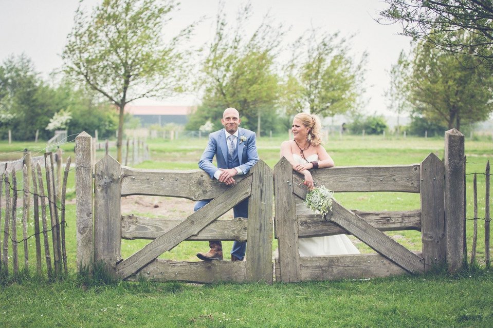 een bruid en bruidegom poseren voor een foto voor een houten hek