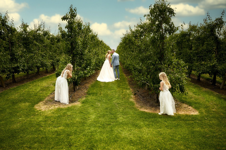 een bruid en bruidegom staan in een appelboomgaard