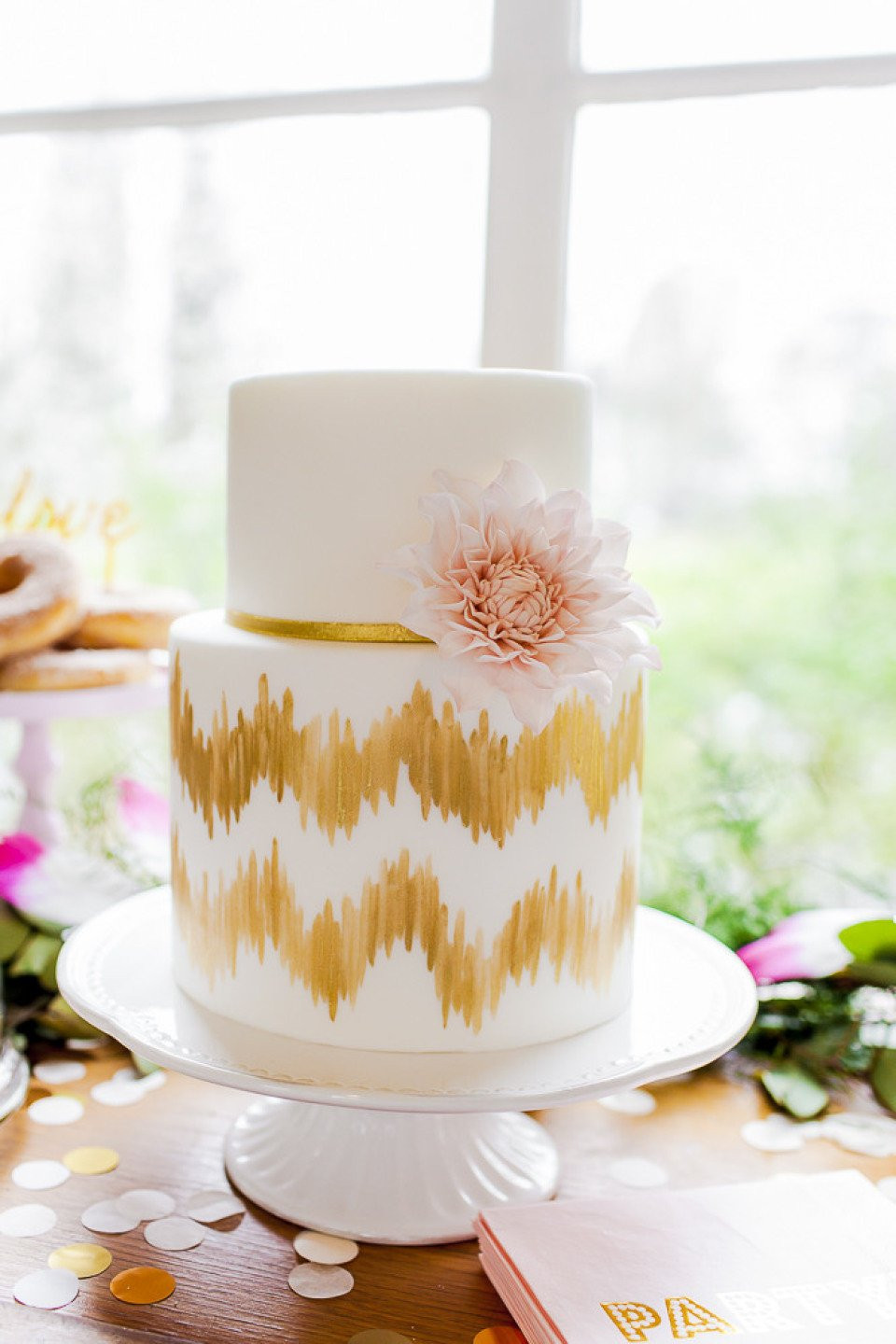 een witte taart met gouden strepen en een roze bloem