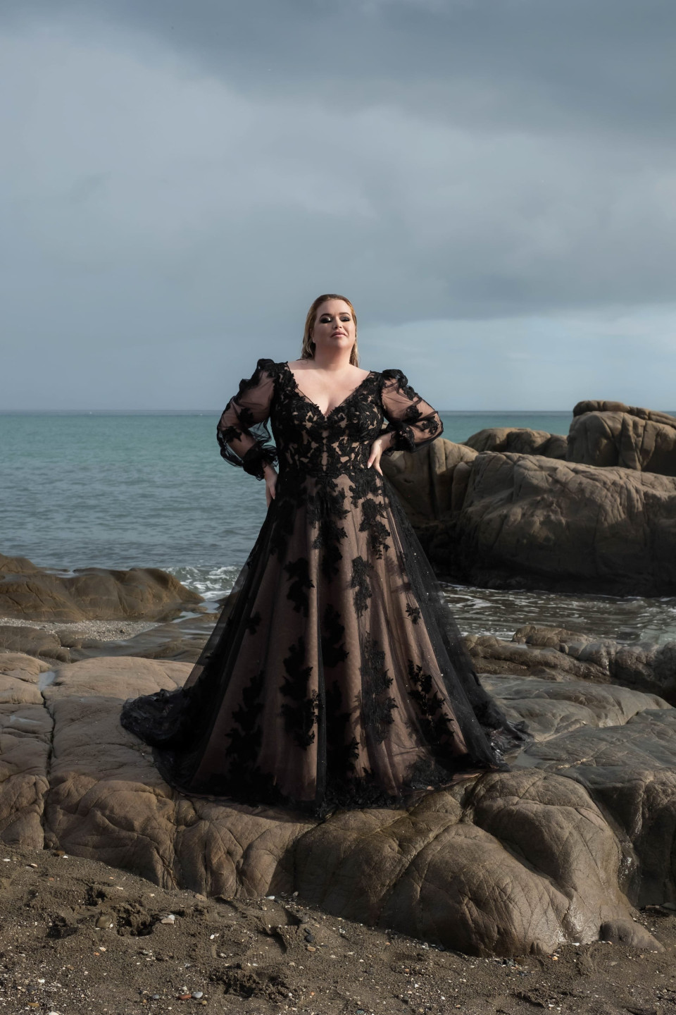 een vrouw in een zwarte trouwjurk die op rotsen staat