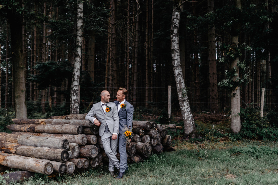 twee bruidegoms staan naast boomstammen in het bos
