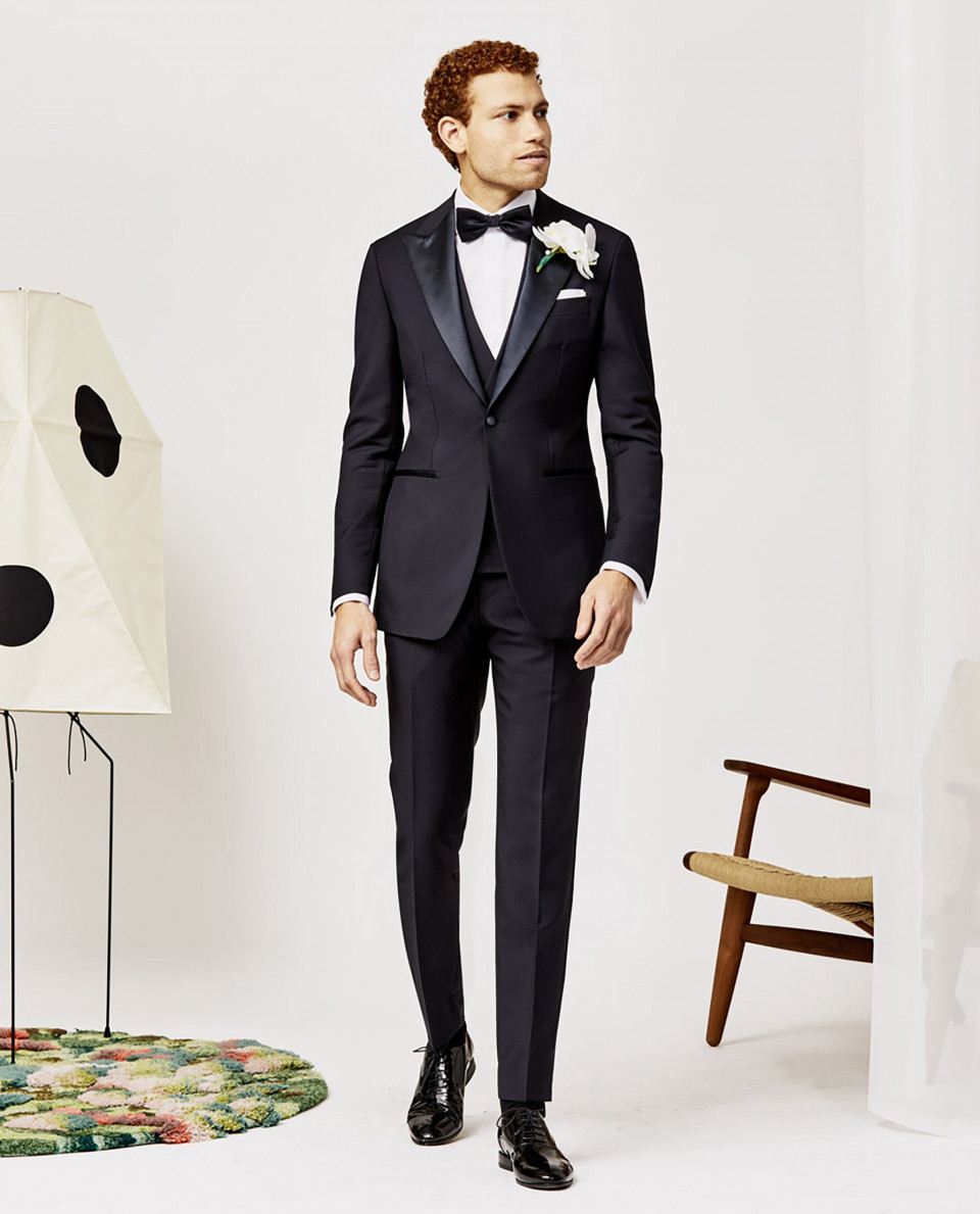 een man in een smoking staat naast een stoel