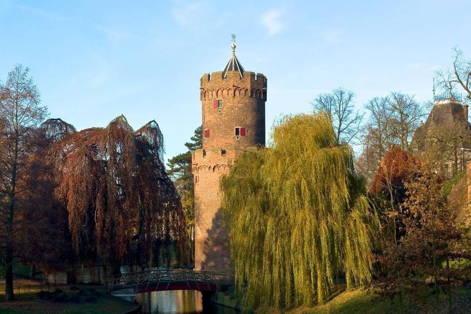 een kasteeltoren is omringd door bomen en een rivier
