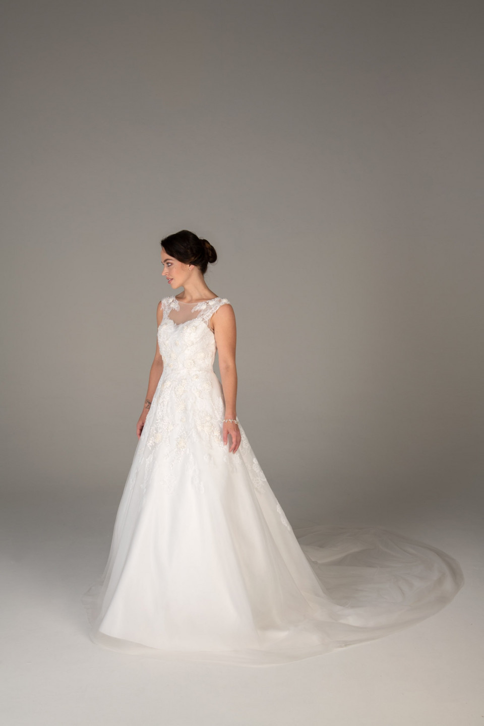 de bruid draagt een bruidsjurk met een doorschijnend, kanten lijfje en een sleep