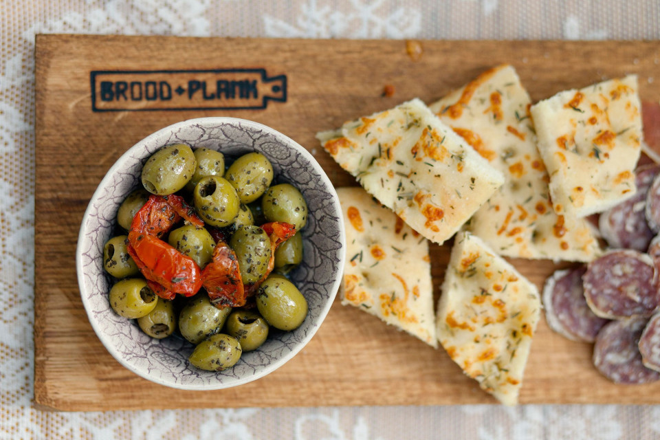 een houten snijplank met olijven, brood en kaas