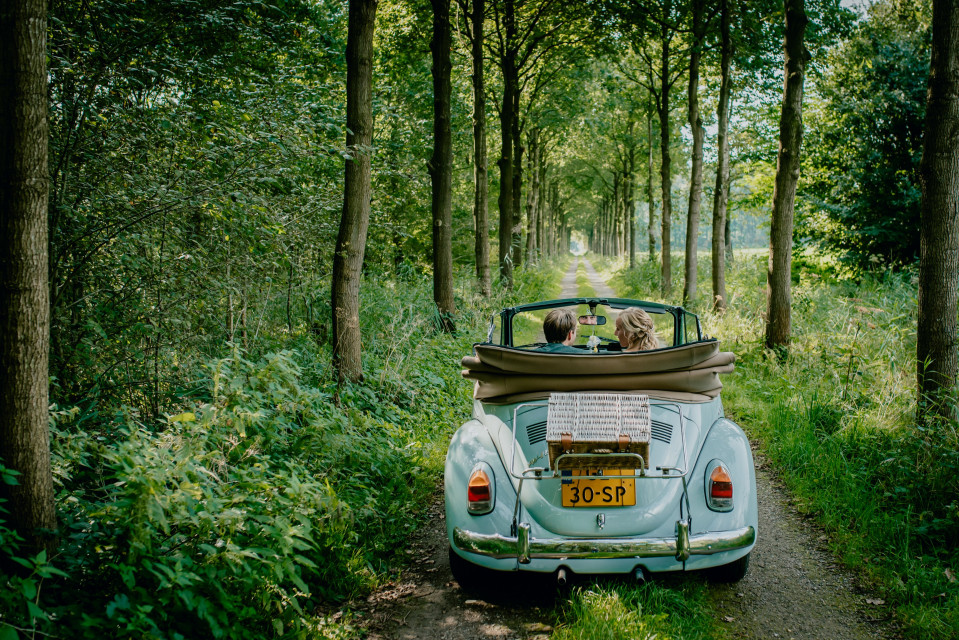 een stel in een vintage auto rijdt door het bos