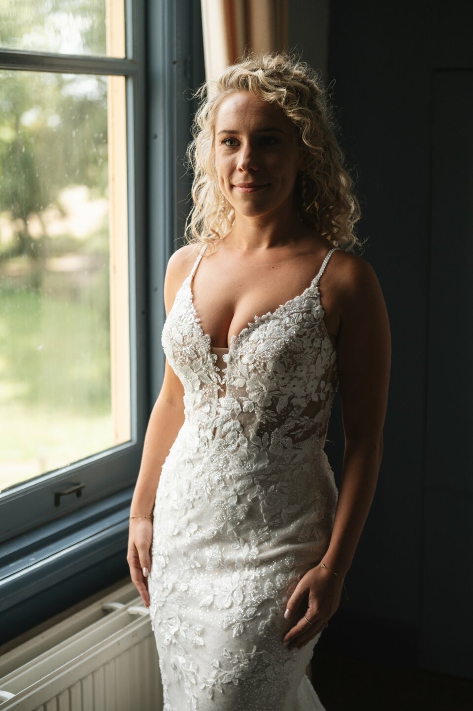 een vrouw in een trouwjurk die voor een raam staat