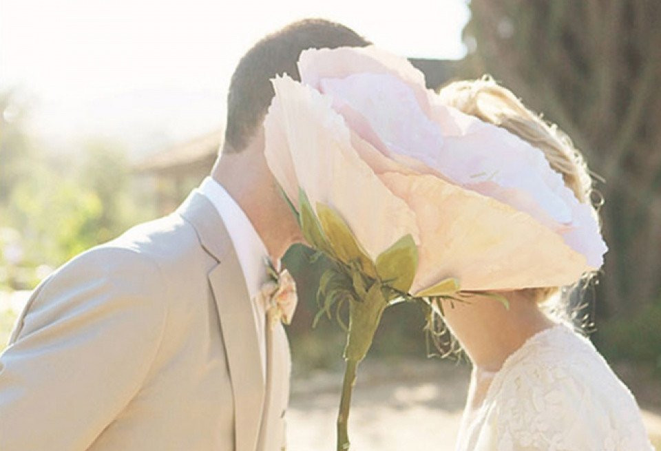 een bruidspaar kust terwijl ze een grote bloem vasthouden
