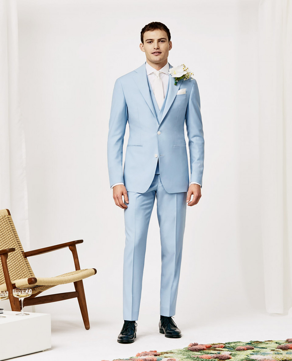 een man in een lichtblauw pak staat voor een stoel