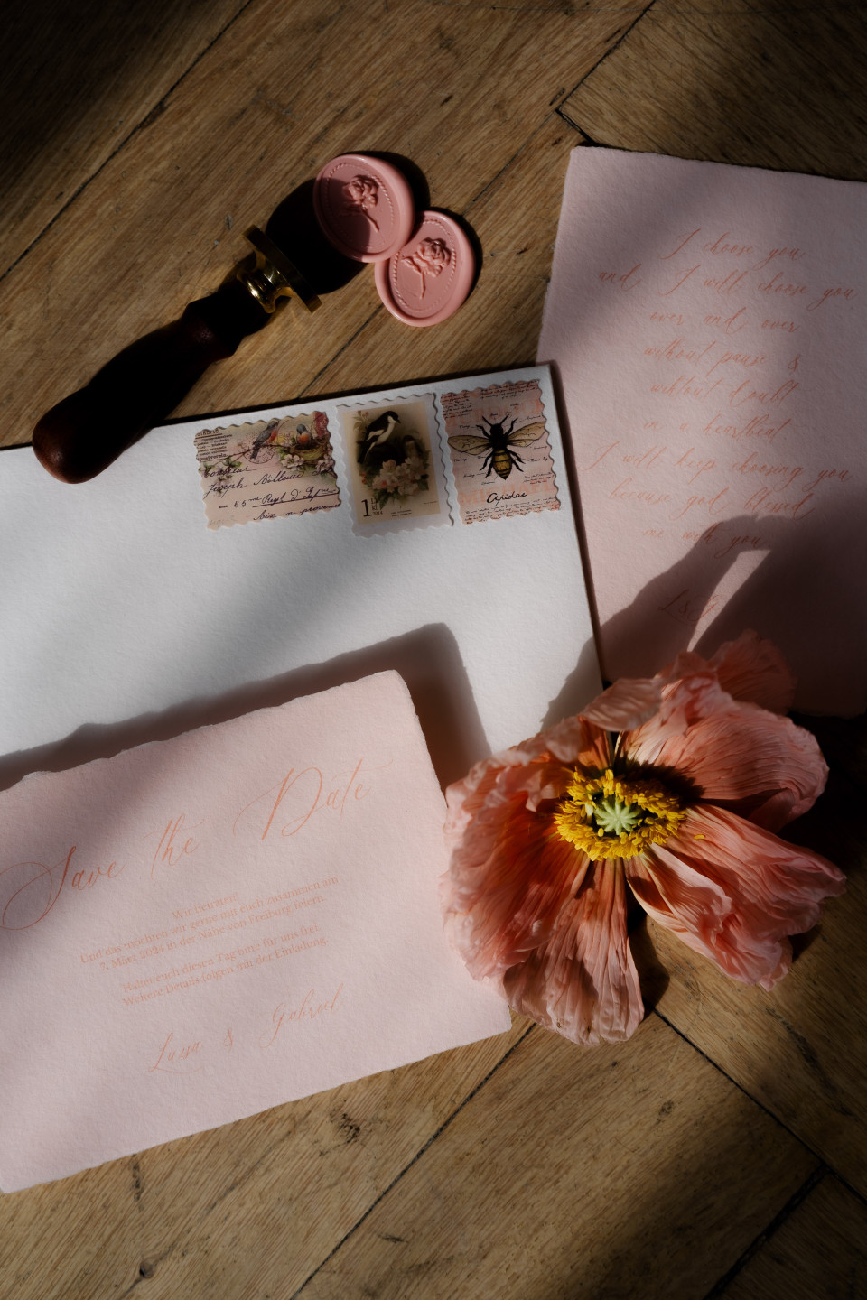 een roze bloem, envelop en postzegel liggen op een houten tafel