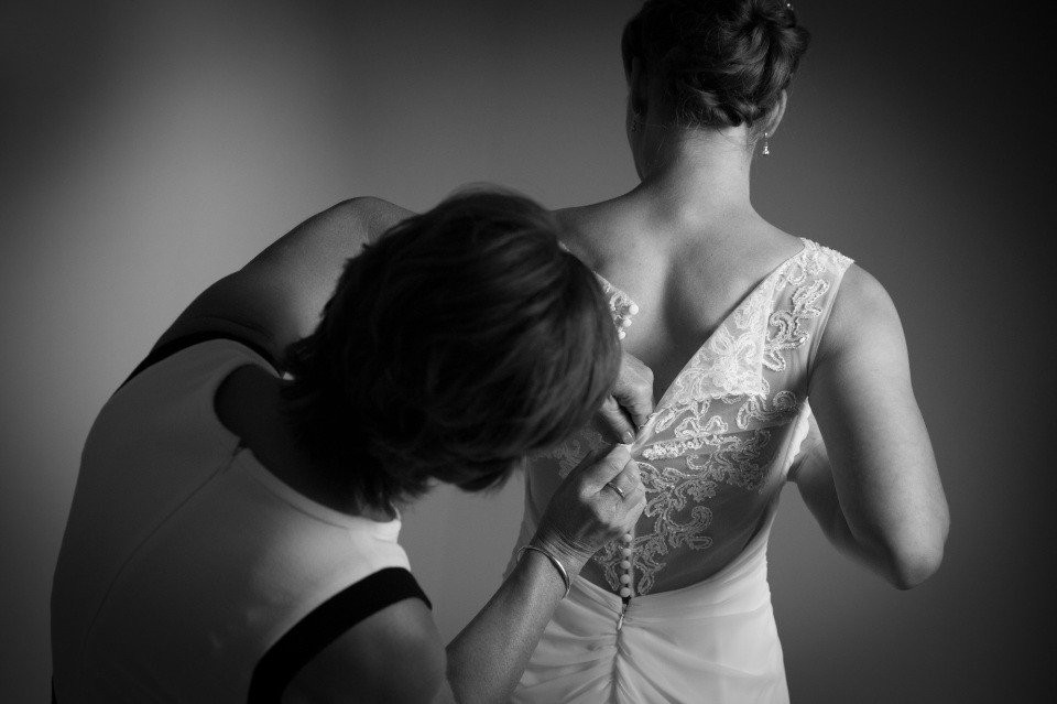 een vrouw helpt een andere vrouw bij het aantrekken van een trouwjurk