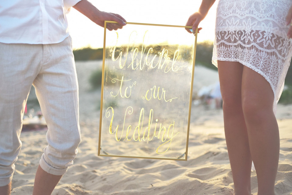 een stel dat een welkomstbord vasthoudt op het strand