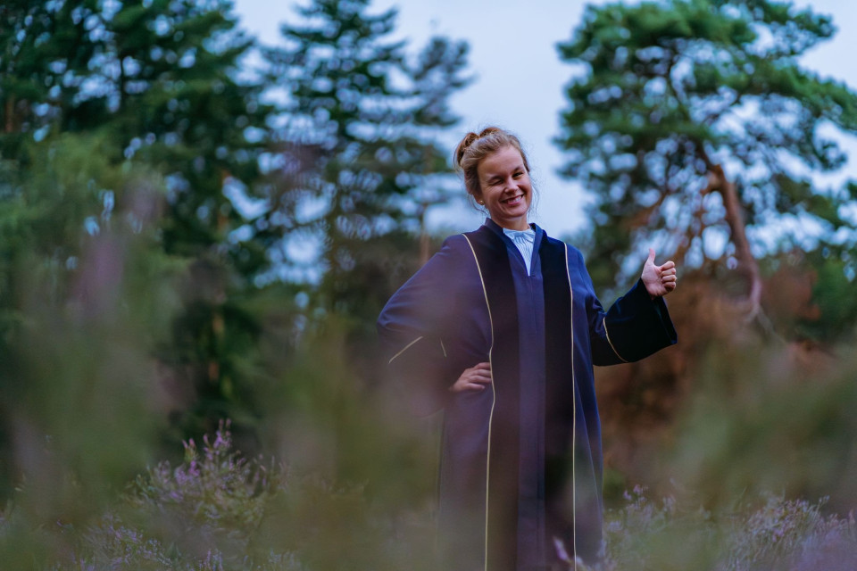 een vrouw in een afstudeer toga staand in een veld