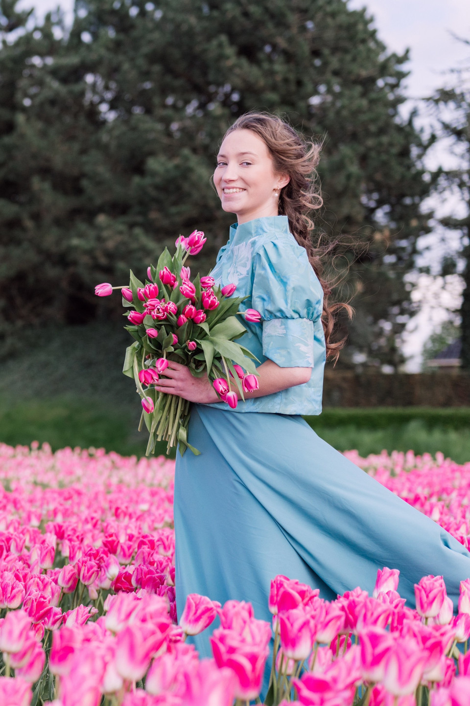 een vrouw in een blauwe jurk die een boeket roze tulpen vasthoudt