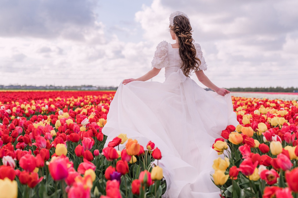 een bruid in een witte jurk die staat in een veld van tulpen