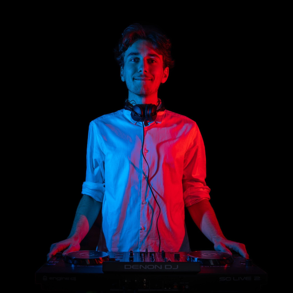 een man in een wit shirt en koptelefoon staat voor een dj-mixer