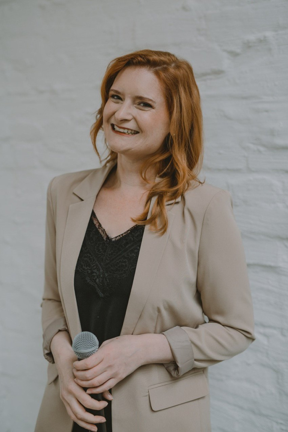 een vrouw met rood haar en een zwart topje en een beige blazer