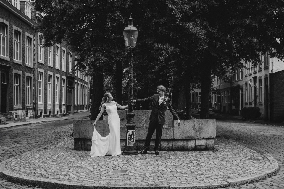 een bruid en bruidegom poseren voor een foto in het midden van een straat met kinderkopjes
