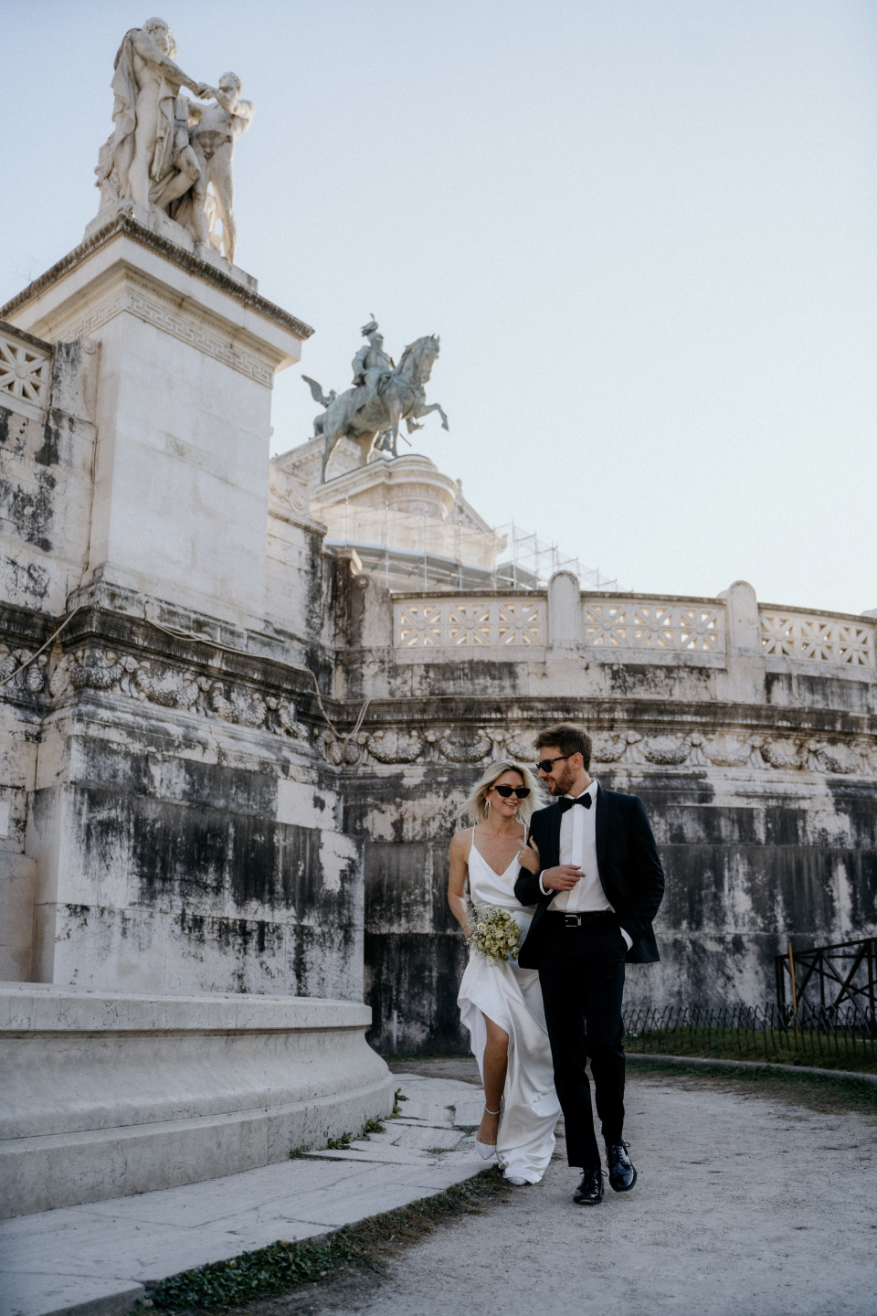 een bruid en bruidegom lopen voor het standbeeld van de keizer in Rome