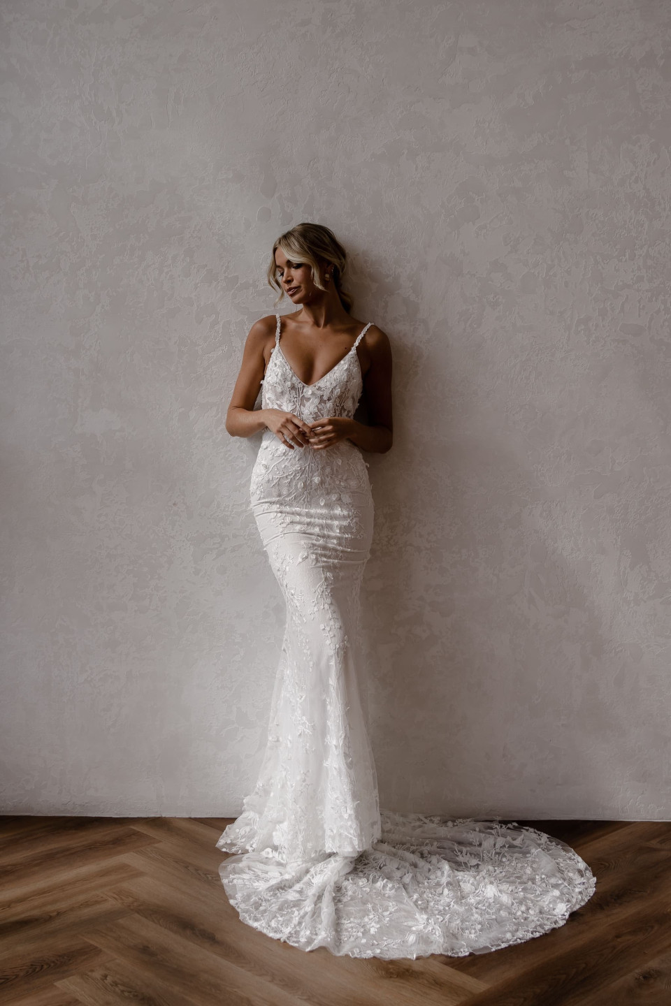 een mooie bruid in een witte trouwjurk leunt tegen een muur