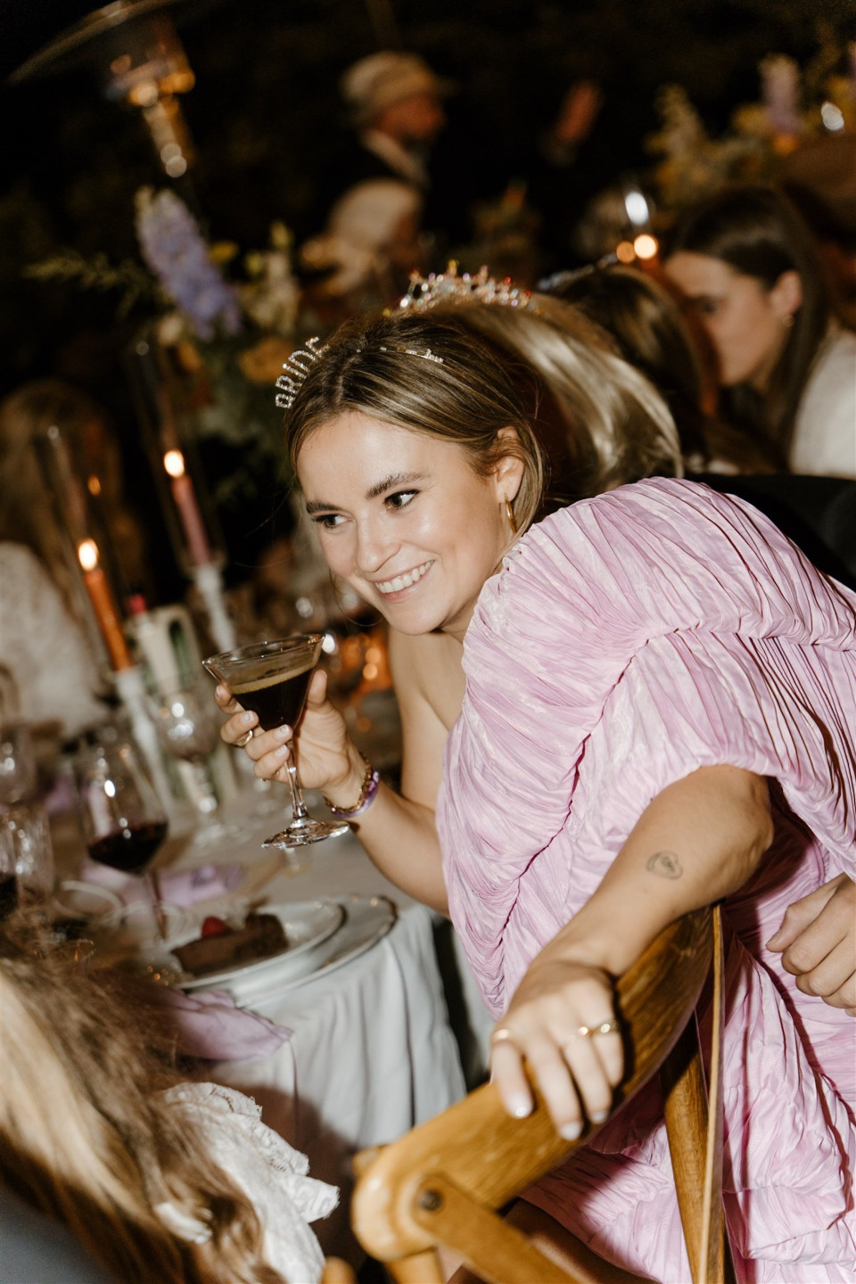 een vrouw in een roze jurk zit aan tafel met andere mensen